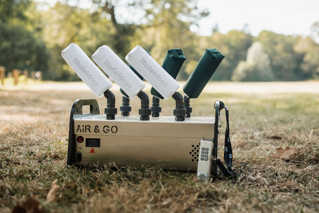 6-Shooter, der air&go Dummylauncher von made4dogs steht in der Natur, auf einer Wiese. Bäume im Hintergrund